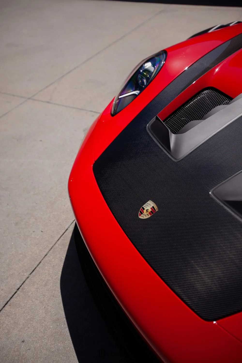 Red Porsche sports car hood with carbon fiber detailing and emblem.