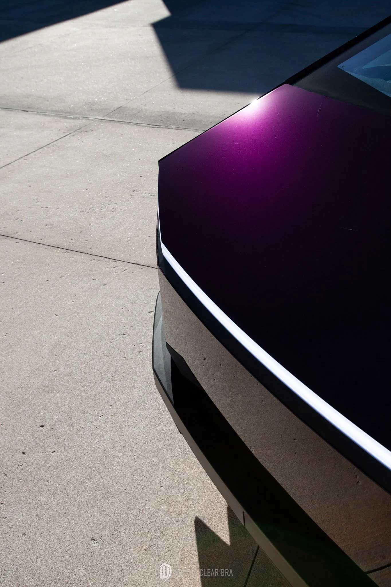 Close-up of a purple car's front corner; white light strip on the edge; on asphalt.