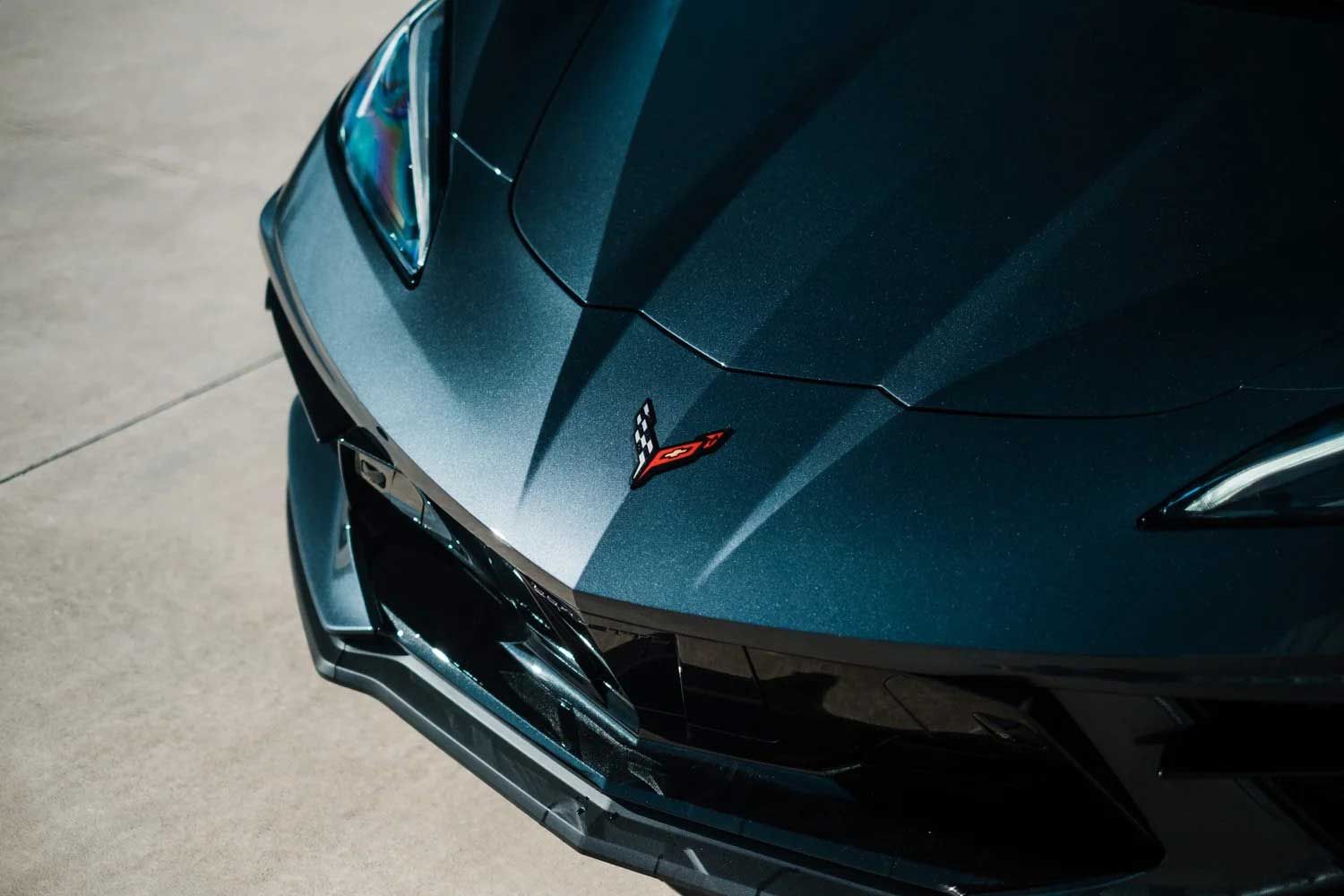 Close-up of a dark gray Chevrolet Corvette's front end, showing the emblem and headlights.