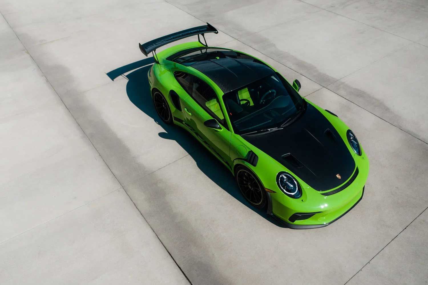Green and black Porsche 911 GT3 RS with a rear wing parked on concrete.