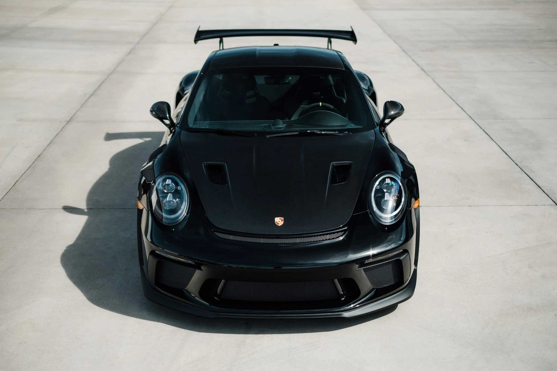 Black Porsche sports car, from a front-facing, elevated perspective, on a concrete surface.