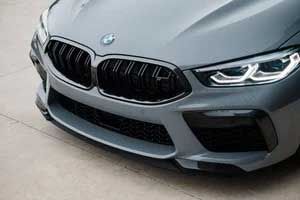 Gray BMW M8's front. Black grille and bumper, BMW logo visible. Headlights on.