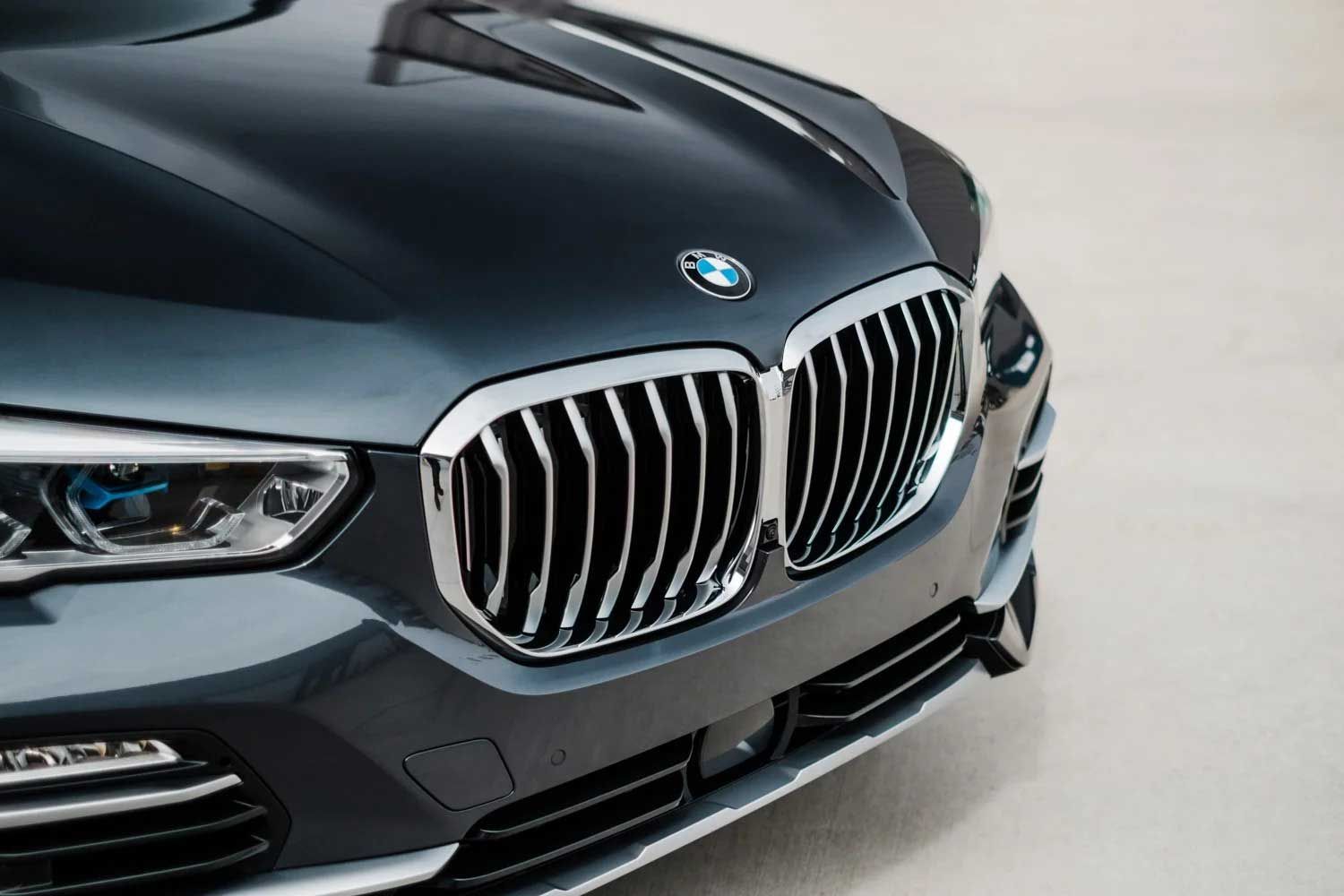 Close-up of a dark grey BMW SUV front end, chrome grill and emblem visible.