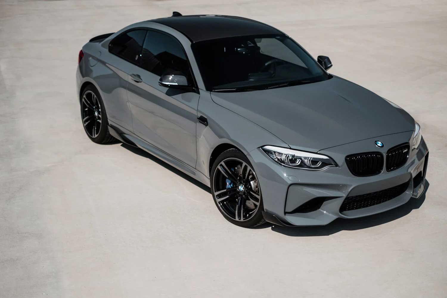 Gray BMW M2 coupe with black roof parked on a concrete surface.