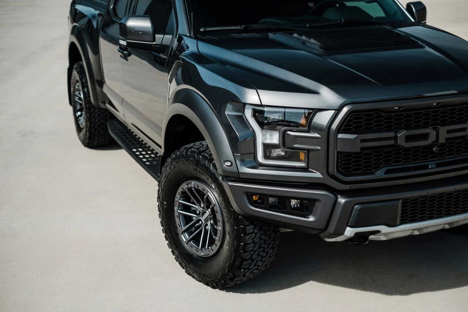 Dark gray Ford Raptor pickup truck, front quarter view, on a light gray surface.