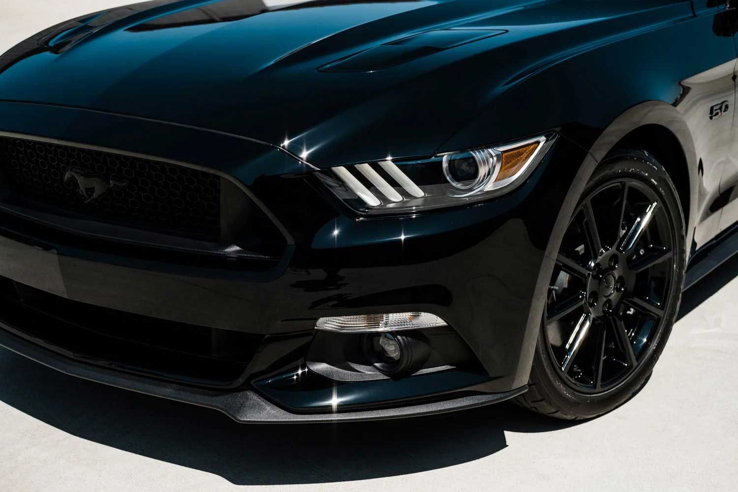 Black Ford Mustang car, front view, shiny paint, black wheels, headlights.