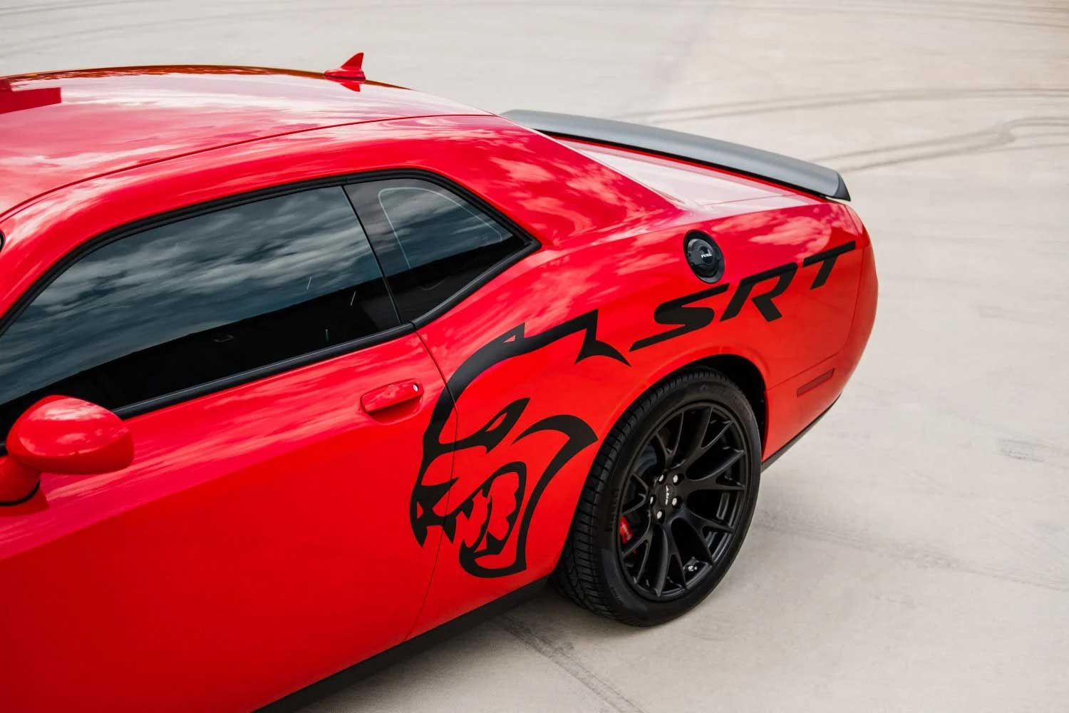 Red Dodge Challenger SRT, black wheels, Hellcat logo, and spoiler on concrete.