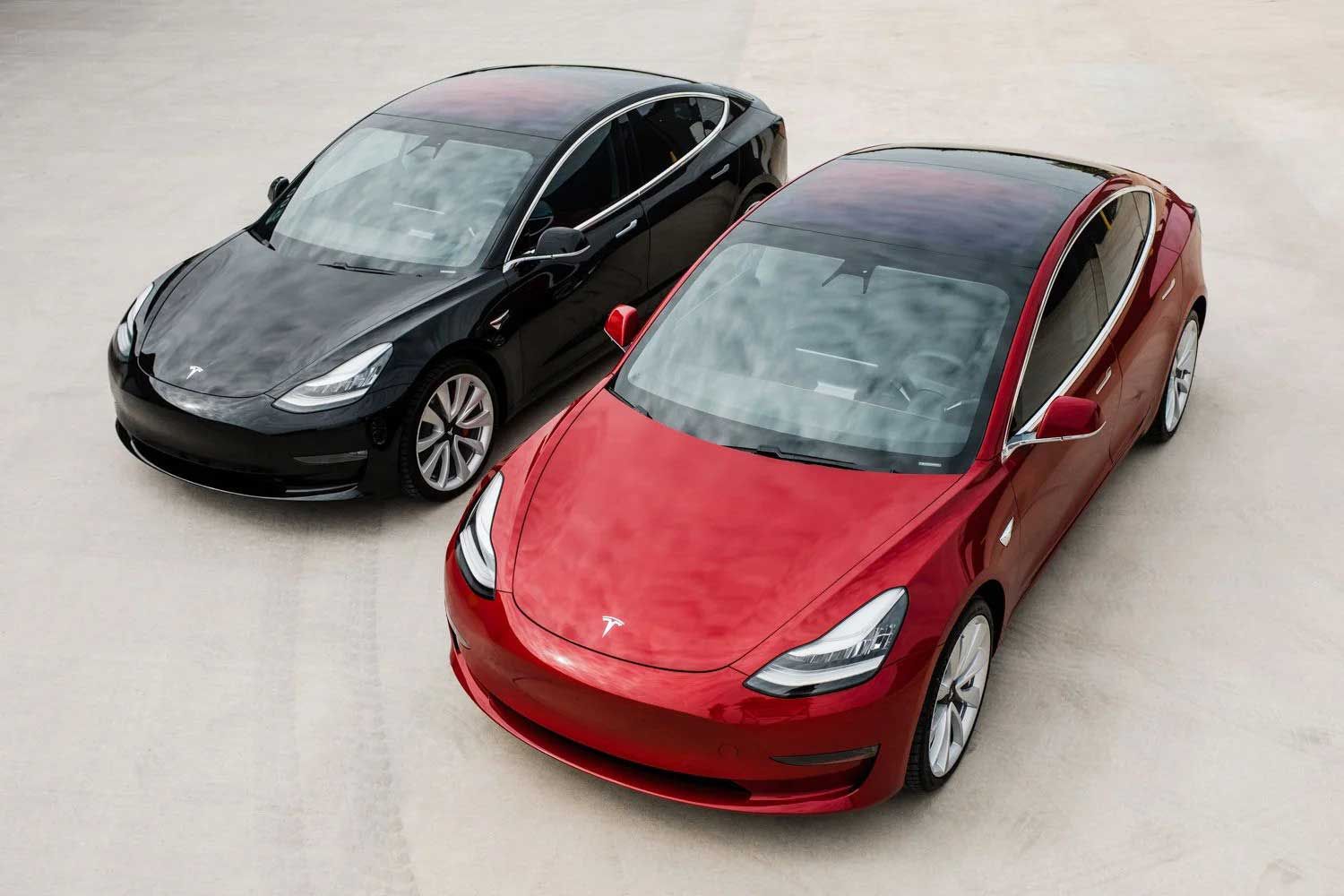 Two Tesla Model 3 cars, one black, one red, parked on a light surface.