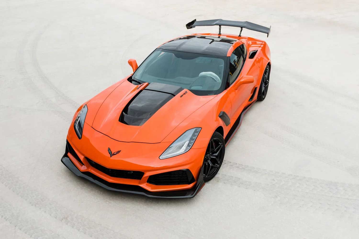 Orange Corvette ZR1 sports car on a light-colored, sandy surface; black accents, rear spoiler.