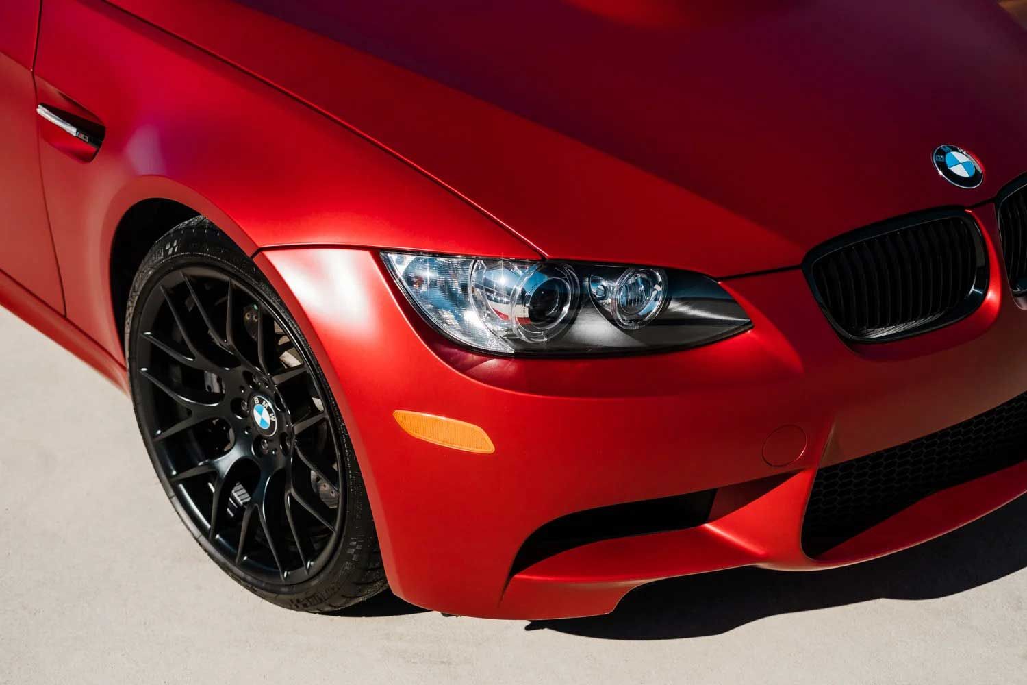 Red BMW M3 coupe, black wheels, close-up of the front, bright headlights, matte finish.