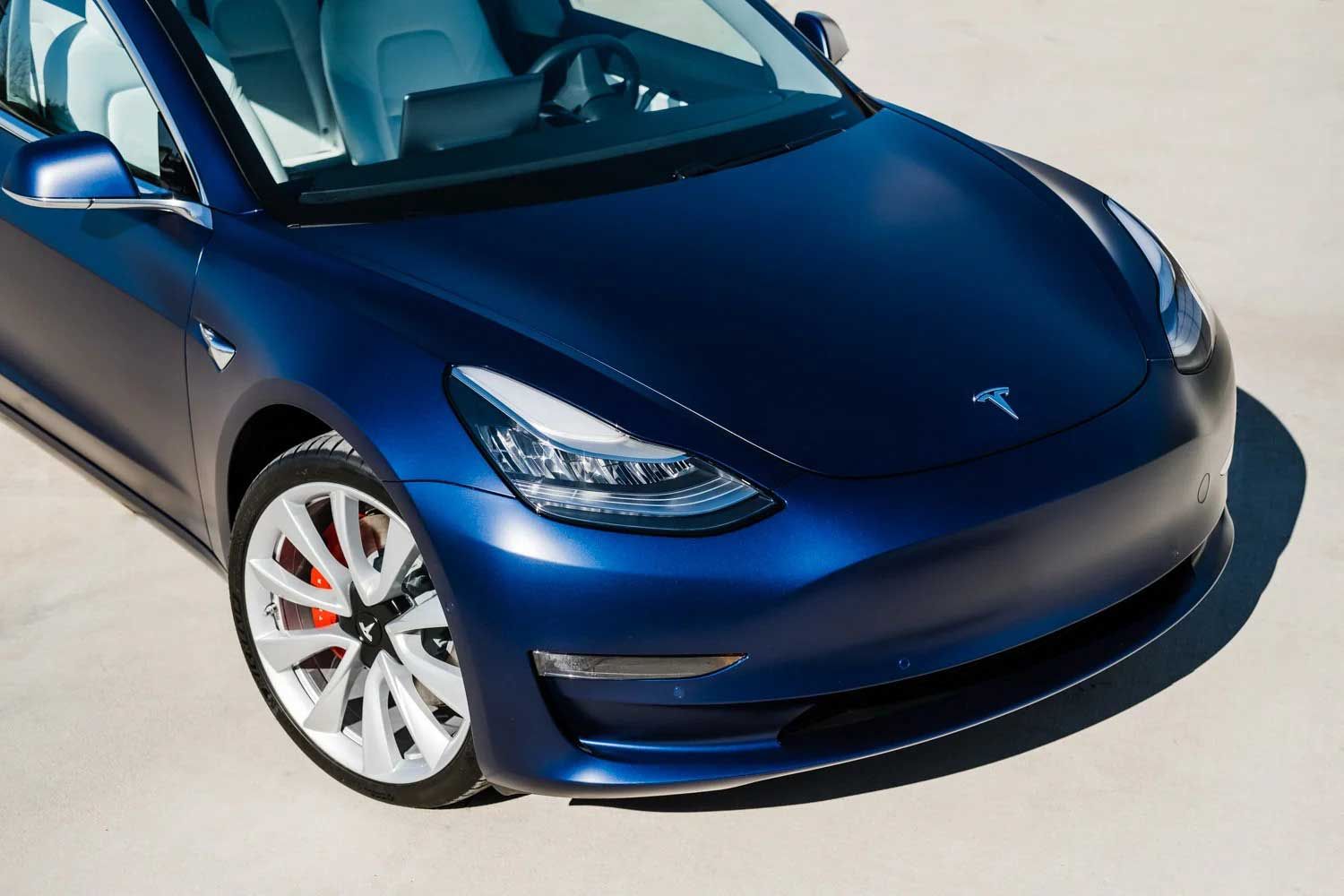 Blue Tesla Model 3 car on a light-colored surface; front view.