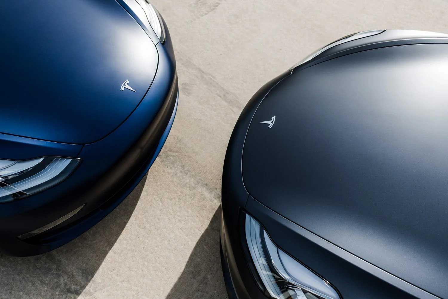 Two blue Tesla Model 3 cars parked close together, hoods facing the camera.