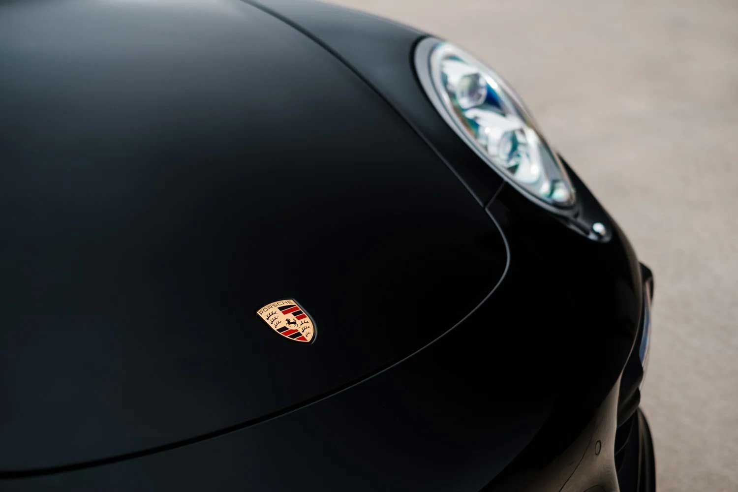 Black Porsche with the brand's logo on the hood and a headlight visible.