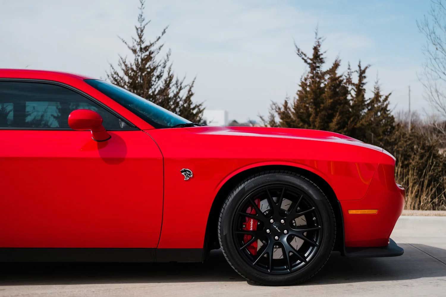 Red Dodge Challenger with black wheels parked outdoors on a sunny day.