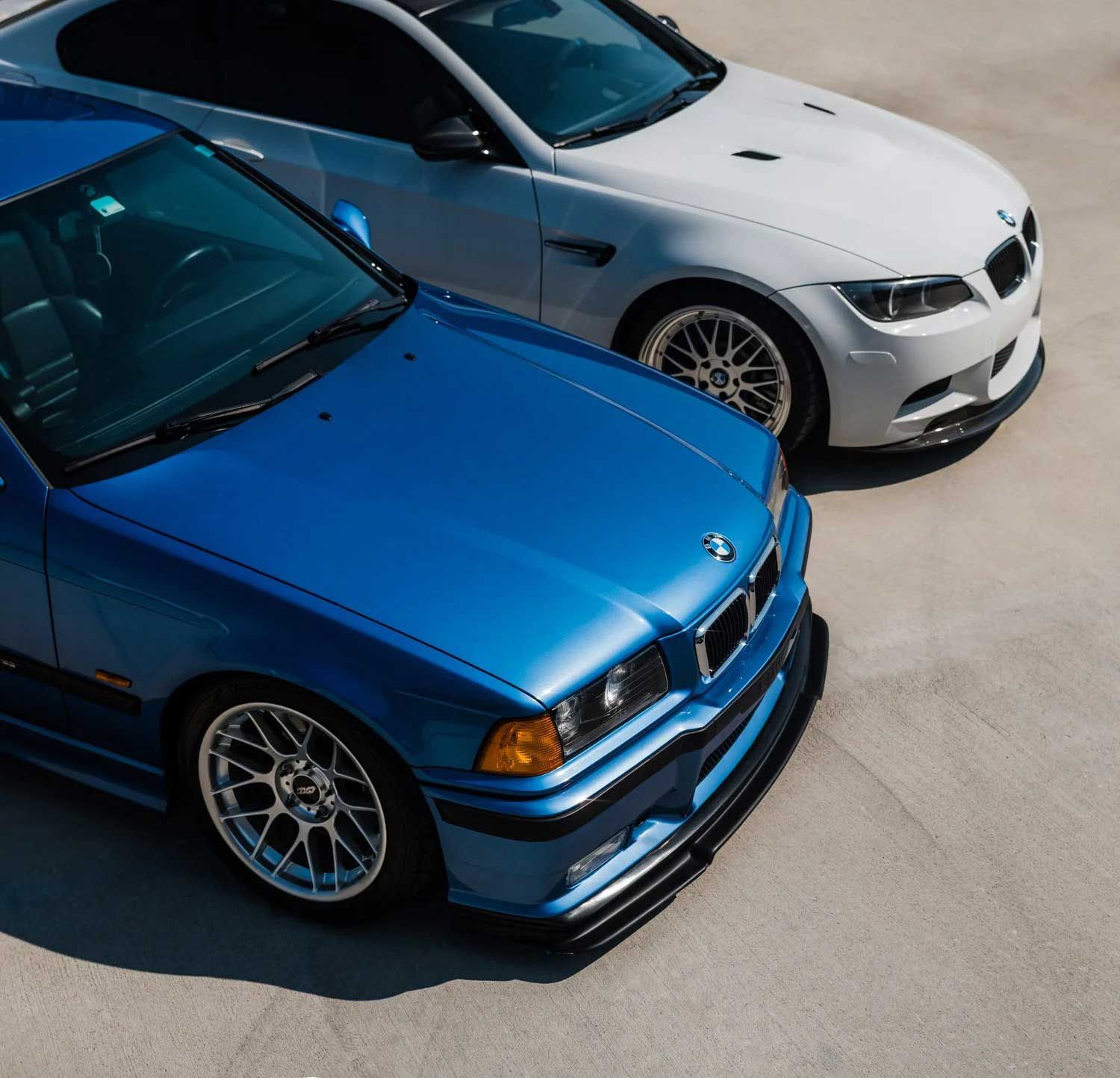 Blue BMW E36 and white BMW E92 parked side by side on a concrete surface.