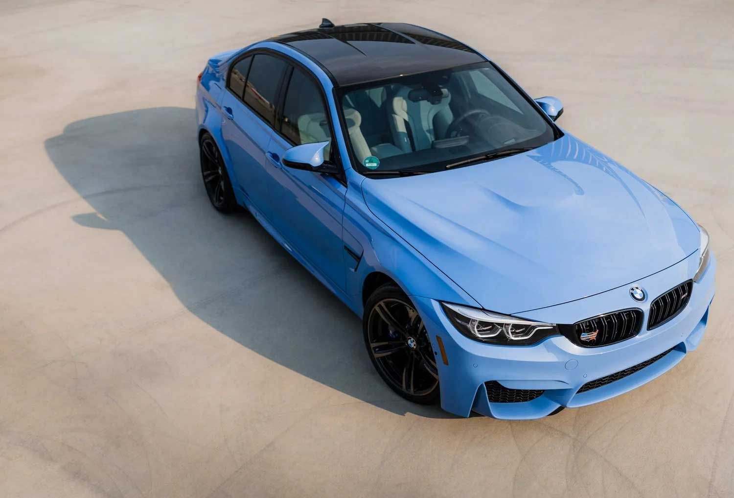 Blue BMW sedan with black roof, parked on a concrete surface.
