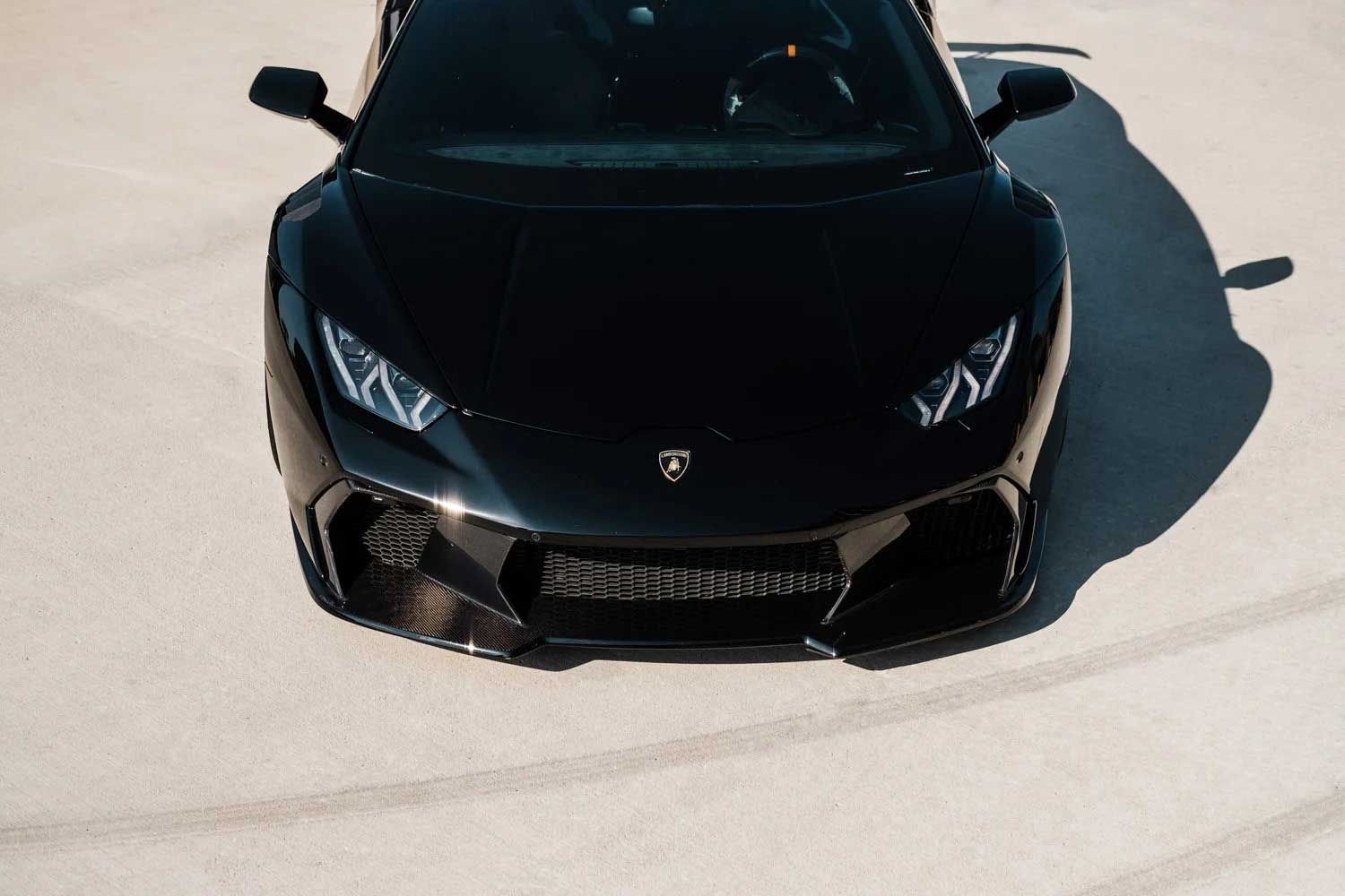 Black Lamborghini Huracan on a bright, concrete surface. Front view.