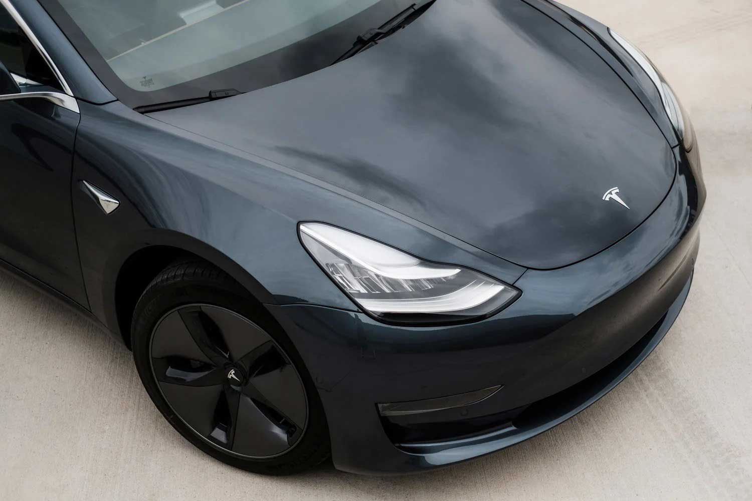 Dark gray Tesla Model 3 car on a concrete surface.