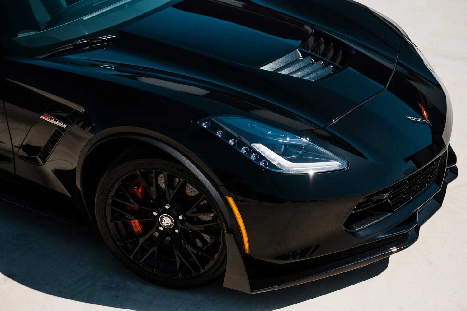Black Chevrolet Corvette sports car, front view. Black wheels, red brake calipers, and a white background.