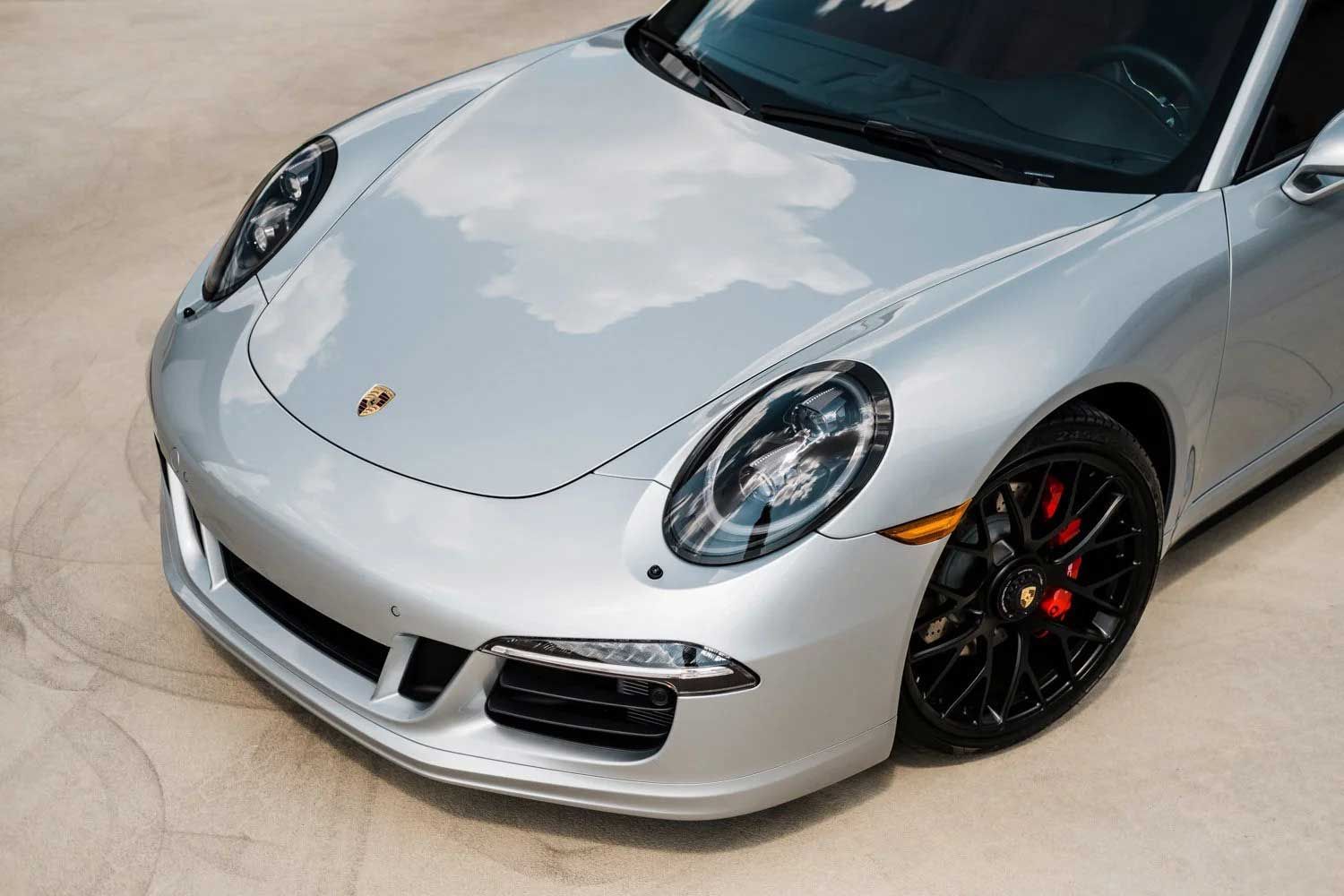 Silver Porsche sports car with black wheels and red brake calipers parked on concrete.