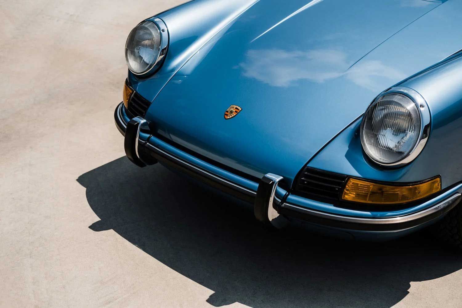 Blue Porsche 911 front end, chrome bumper, yellow turn signals, reflecting the sky.