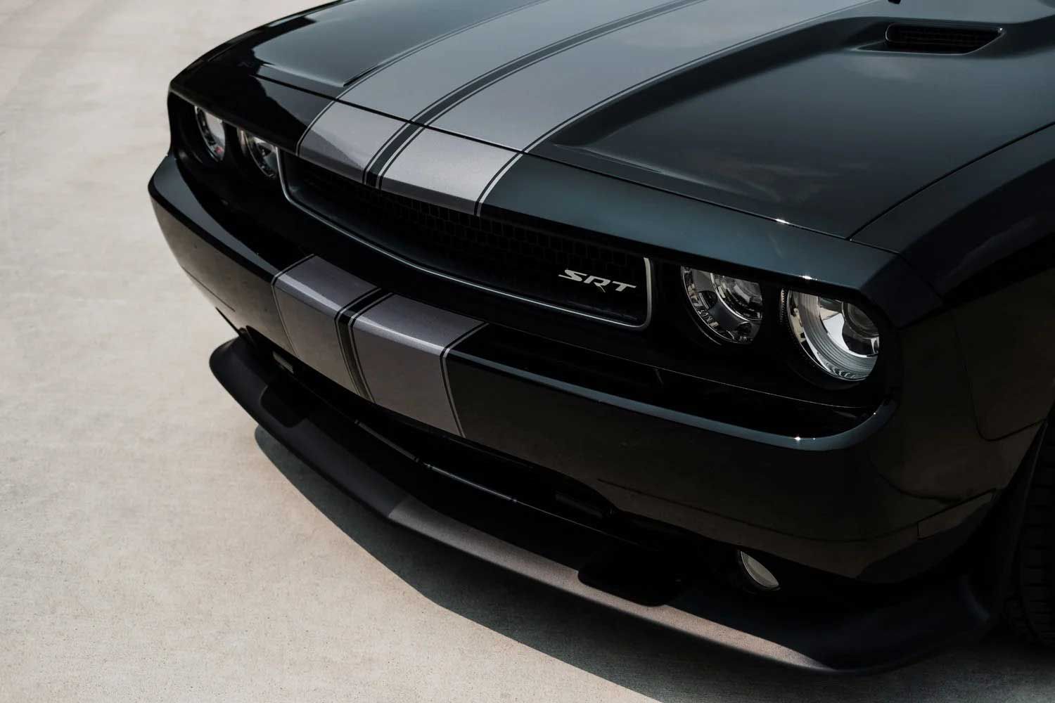 Black Dodge Challenger with gray racing stripes on a light-colored surface.