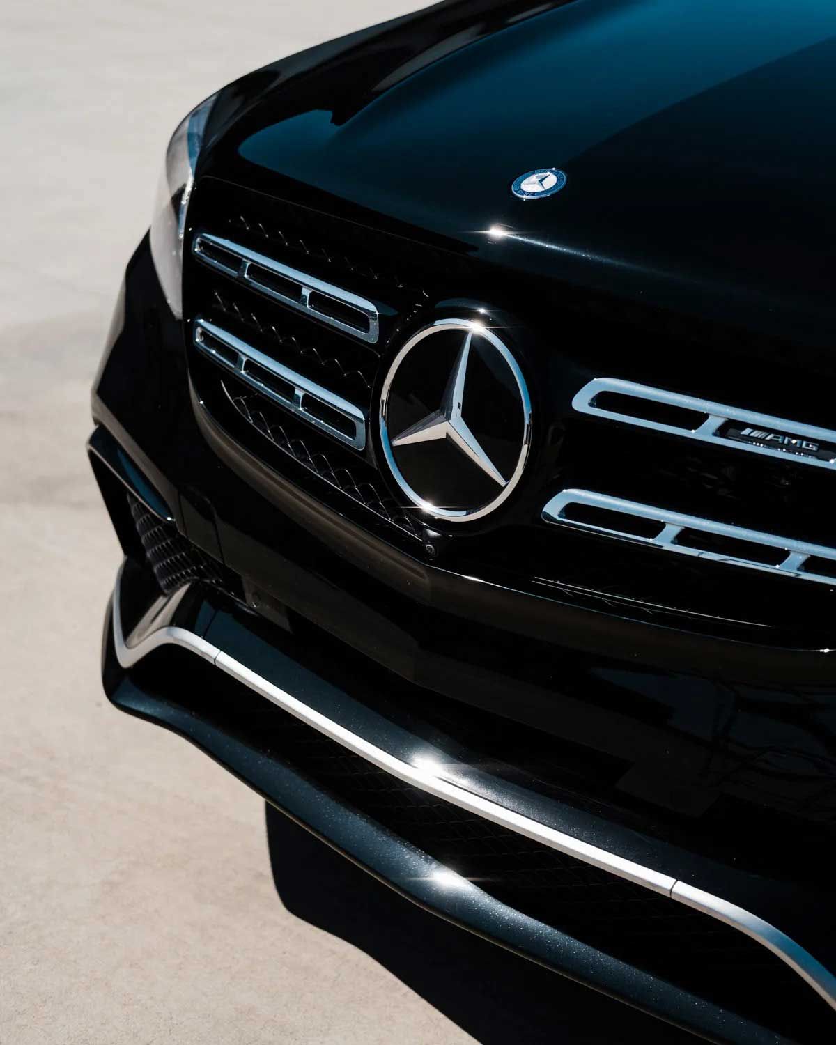 Black Mercedes-Benz front end with prominent emblem and grille detail, parked on light gray surface.