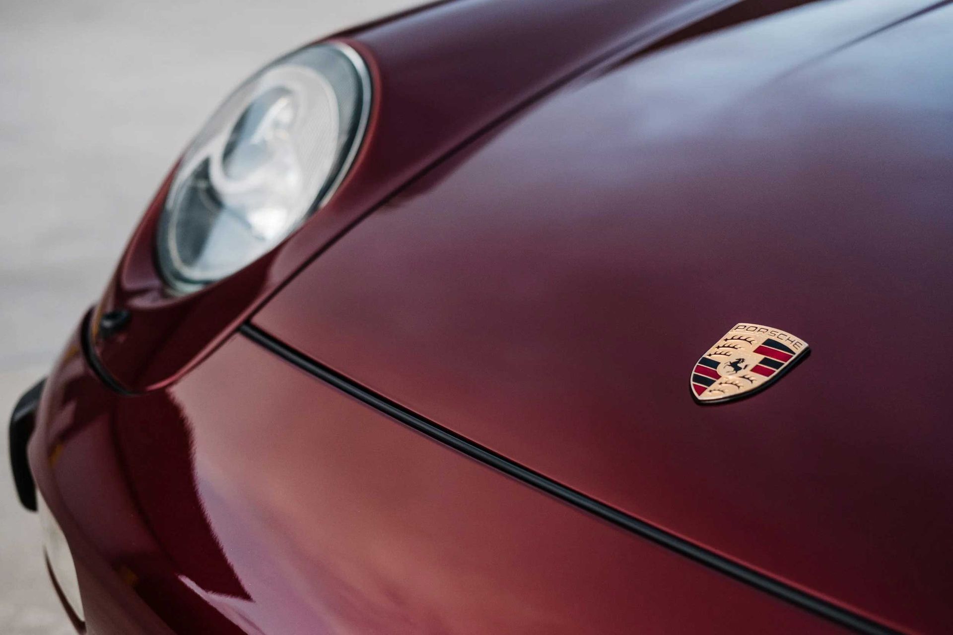 Maroon Porsche hood with emblem and headlight.