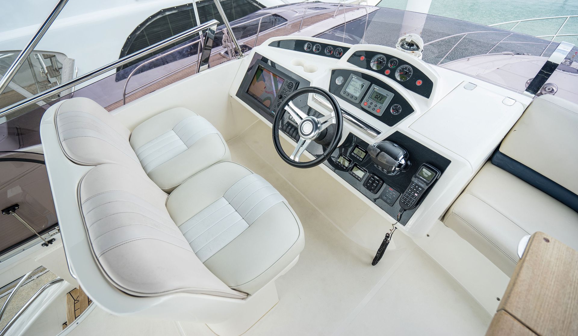 White yacht helm with cushioned seats, steering wheel, and dashboard controls inside a bright cockpit