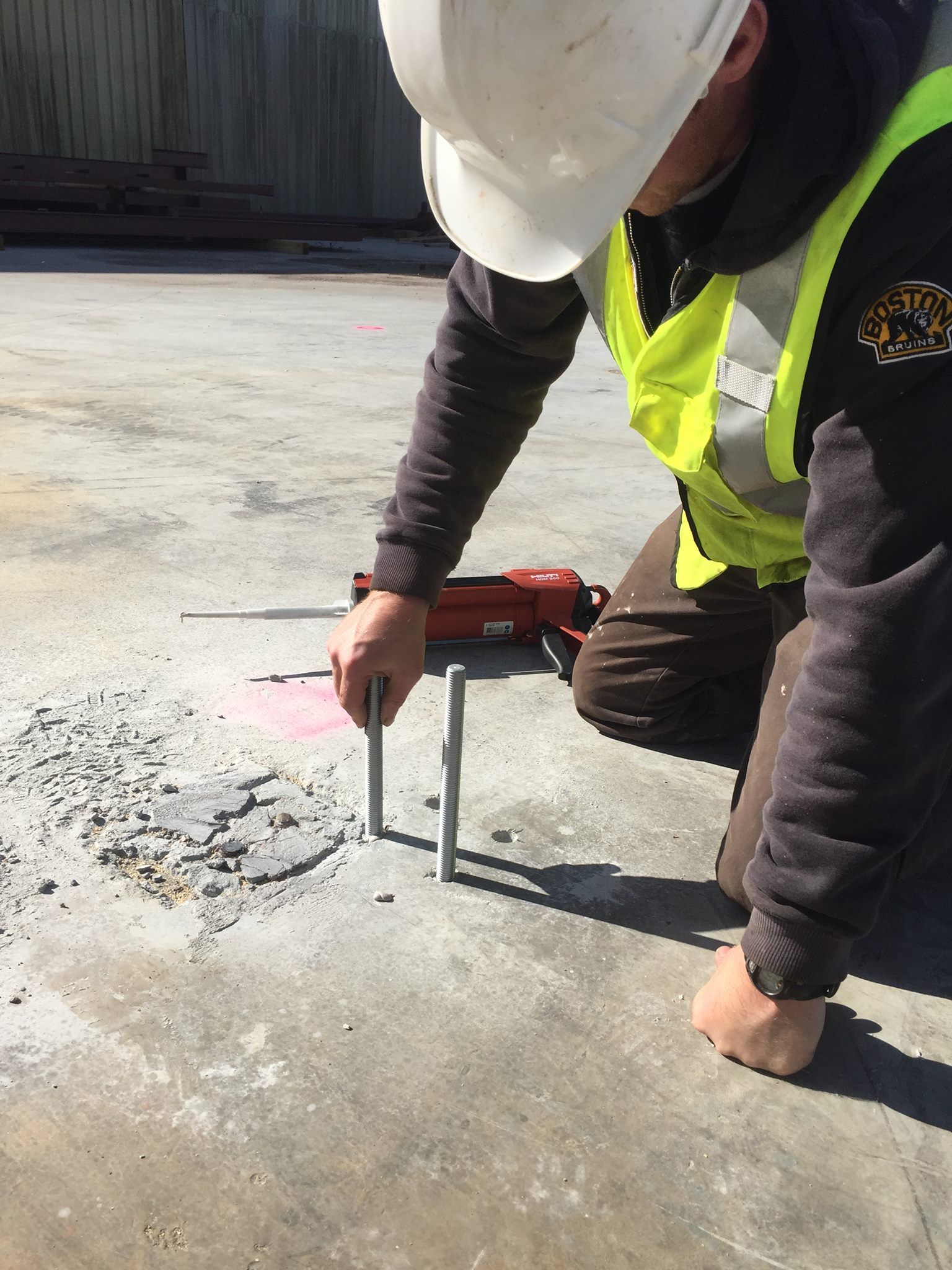 A man wearing a hard hat and safety vest is working on a concrete surface.