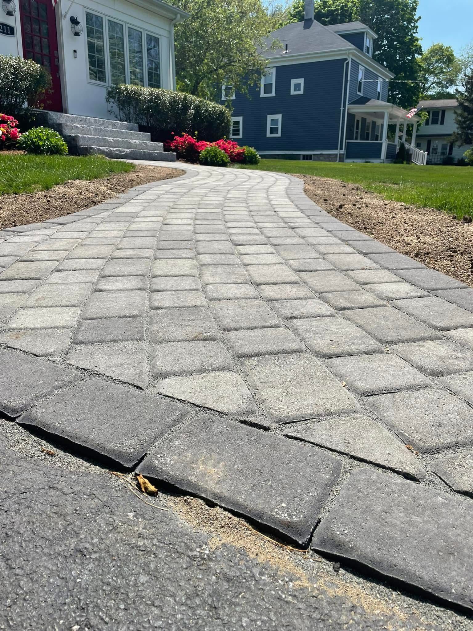 A brick walkway leading to a house with a blue house in the background.
