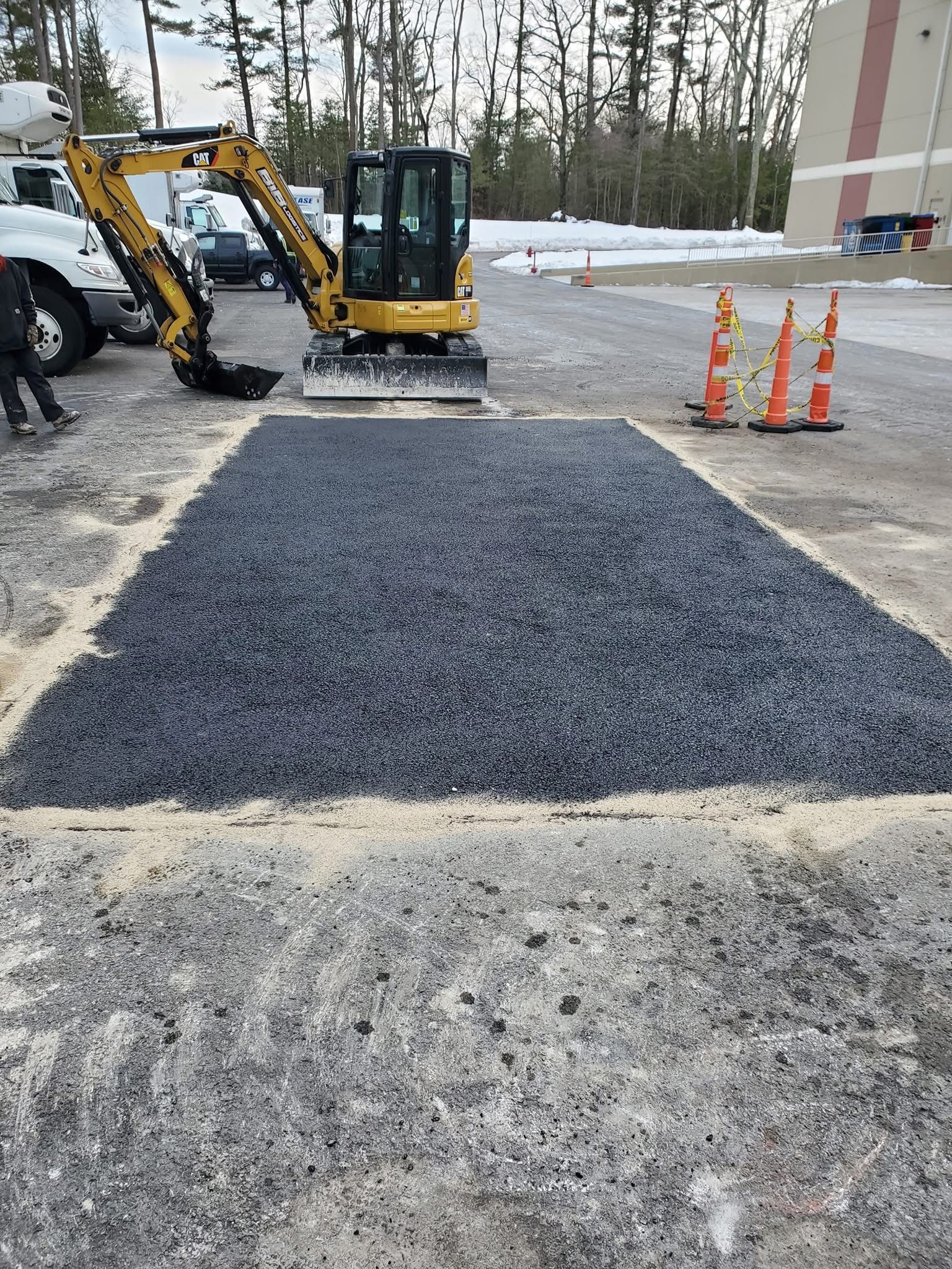 A yellow excavator is digging a hole in the ground in a parking lot.