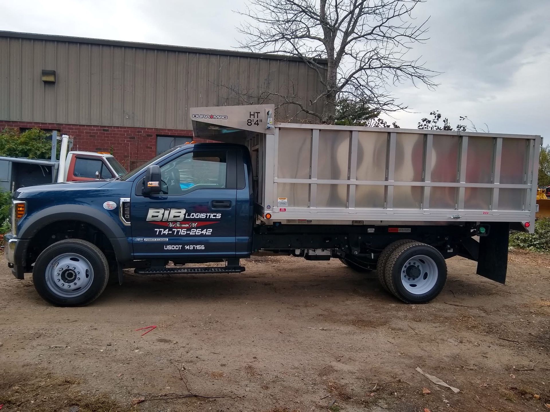 A blue dump truck is parked in a dirt lot in front of a building.