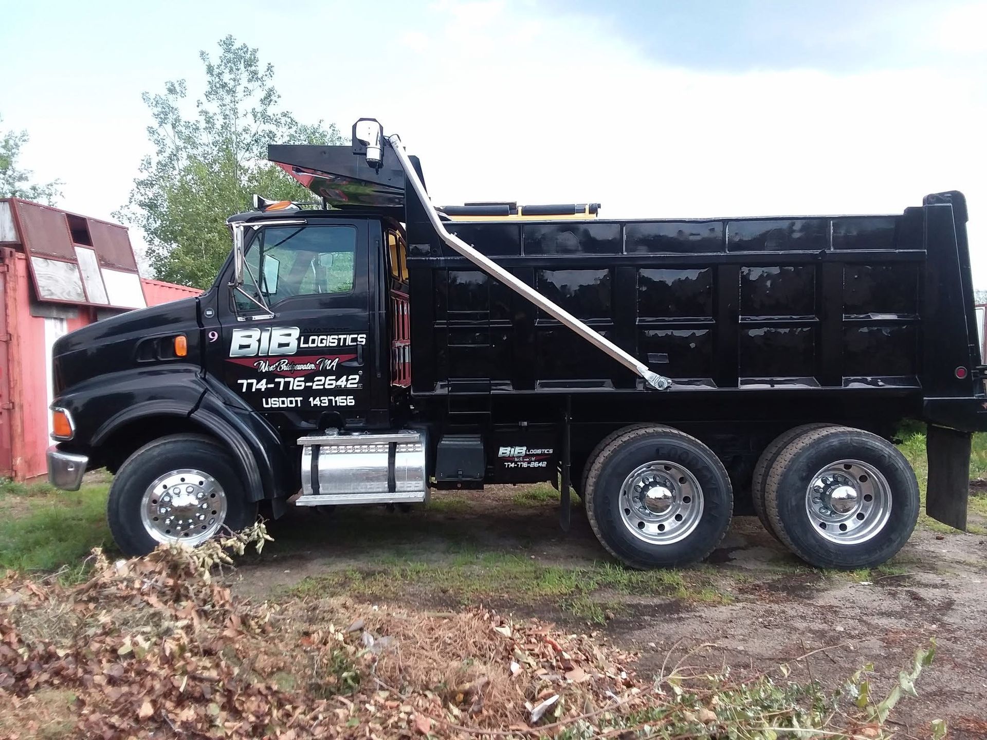 A black dump truck is parked in a grassy field.