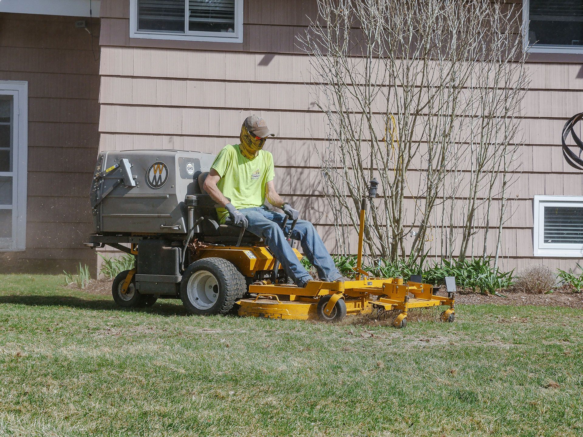 A man is riding a yellow lawn mower on a lush green lawn.