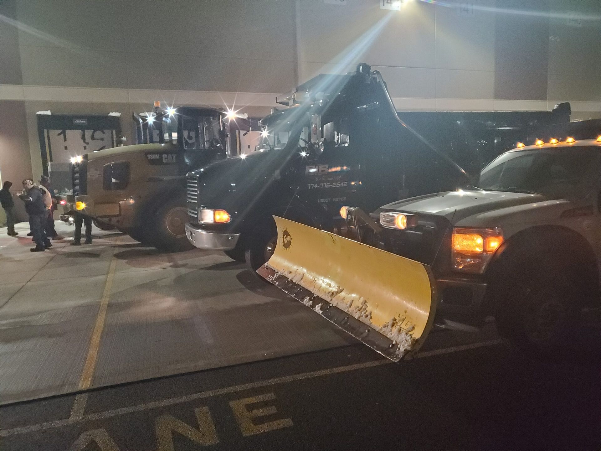 A snow plow is parked next to a truck in a parking lot