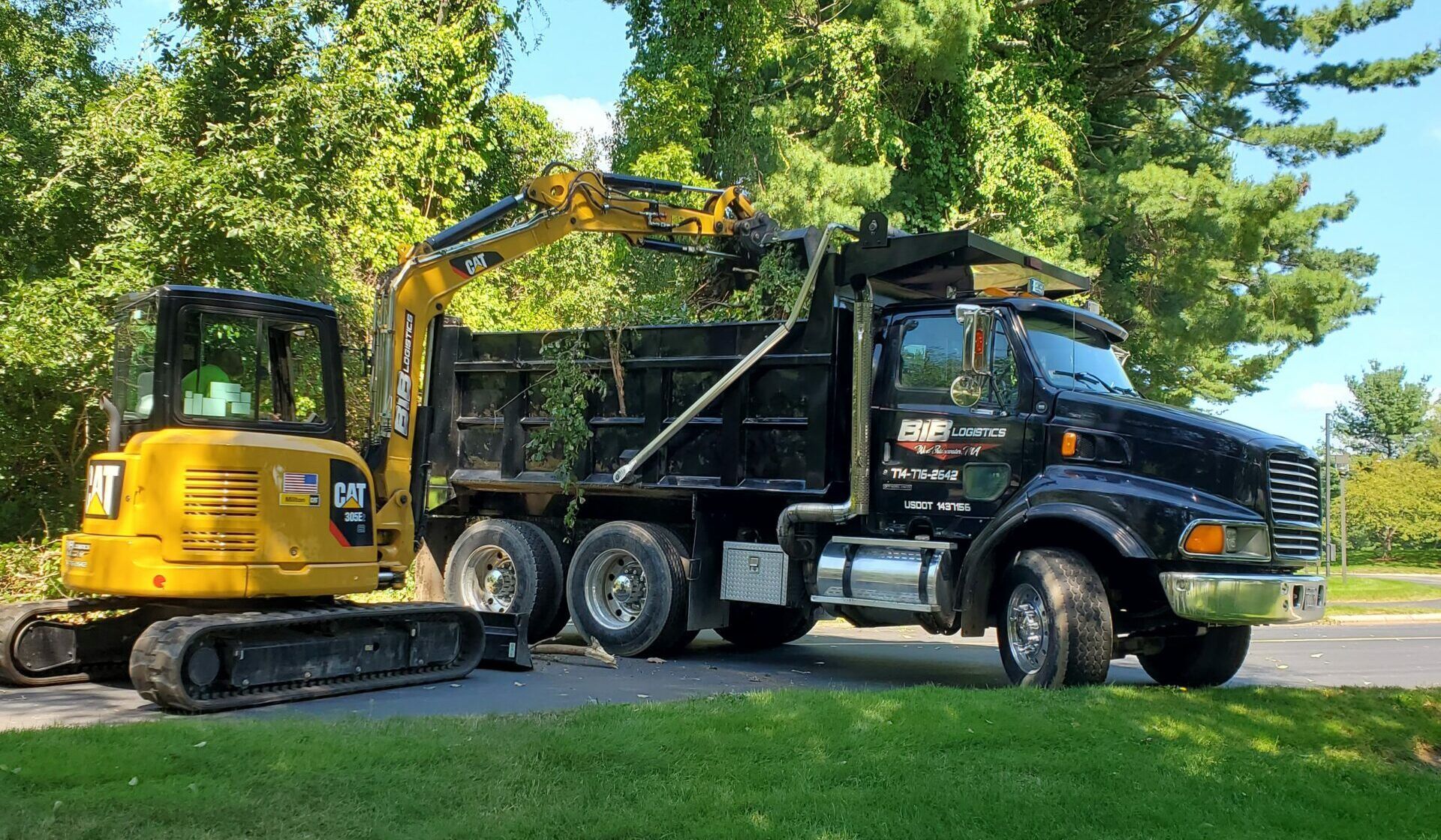A dump truck with a yellow excavator attached to it is parked on the side of the road.