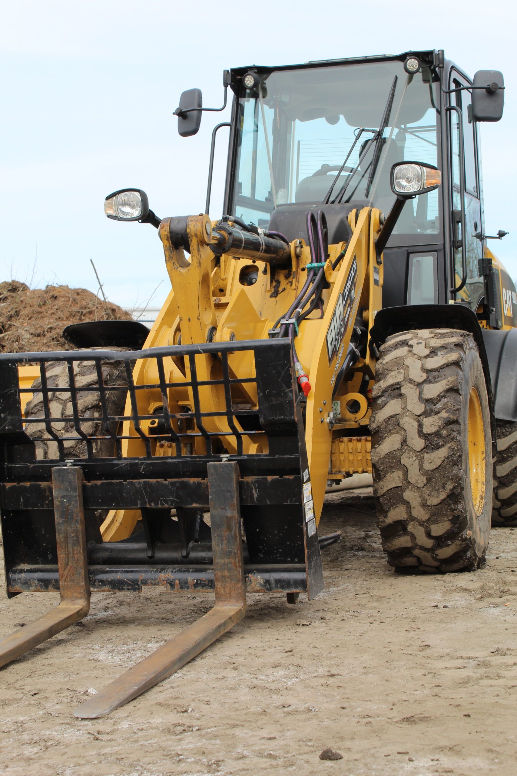 A yellow tractor with forks attached to it is parked in the dirt.