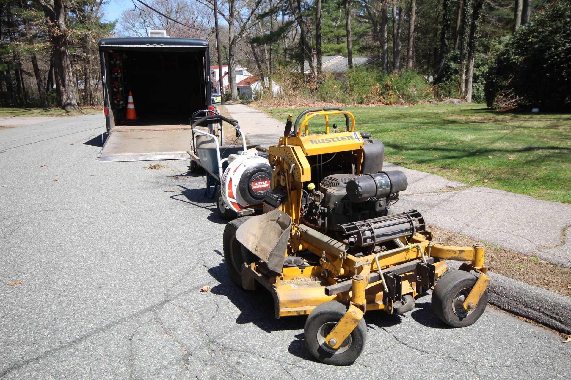 A yellow lawn mower is parked next to a trailer