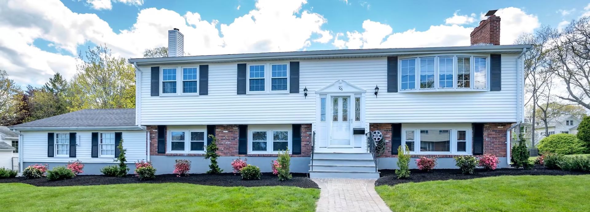 A large white house with black shutters is sitting on top of a lush green lawn.