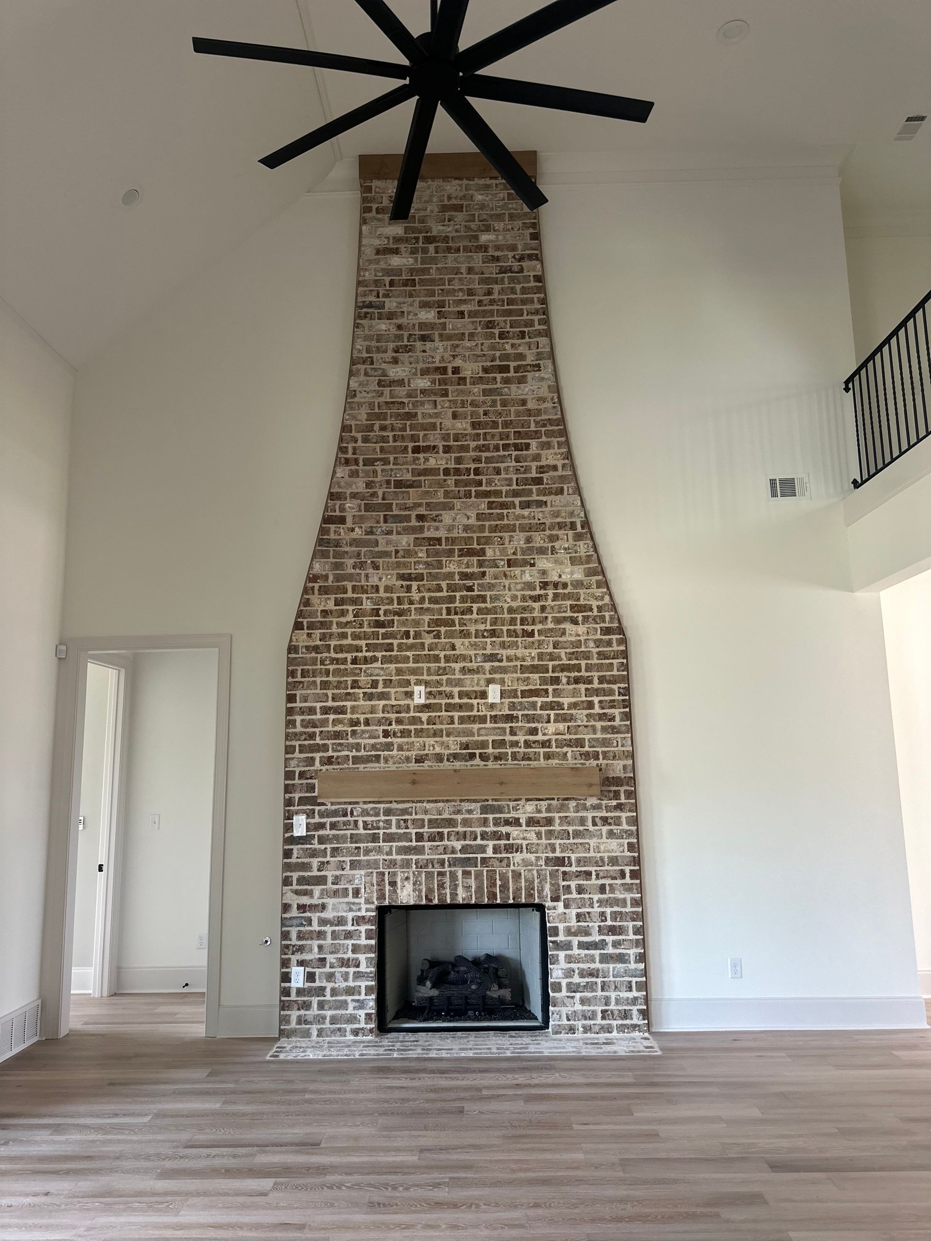 An empty living room with a brick fireplace and a ceiling fan.