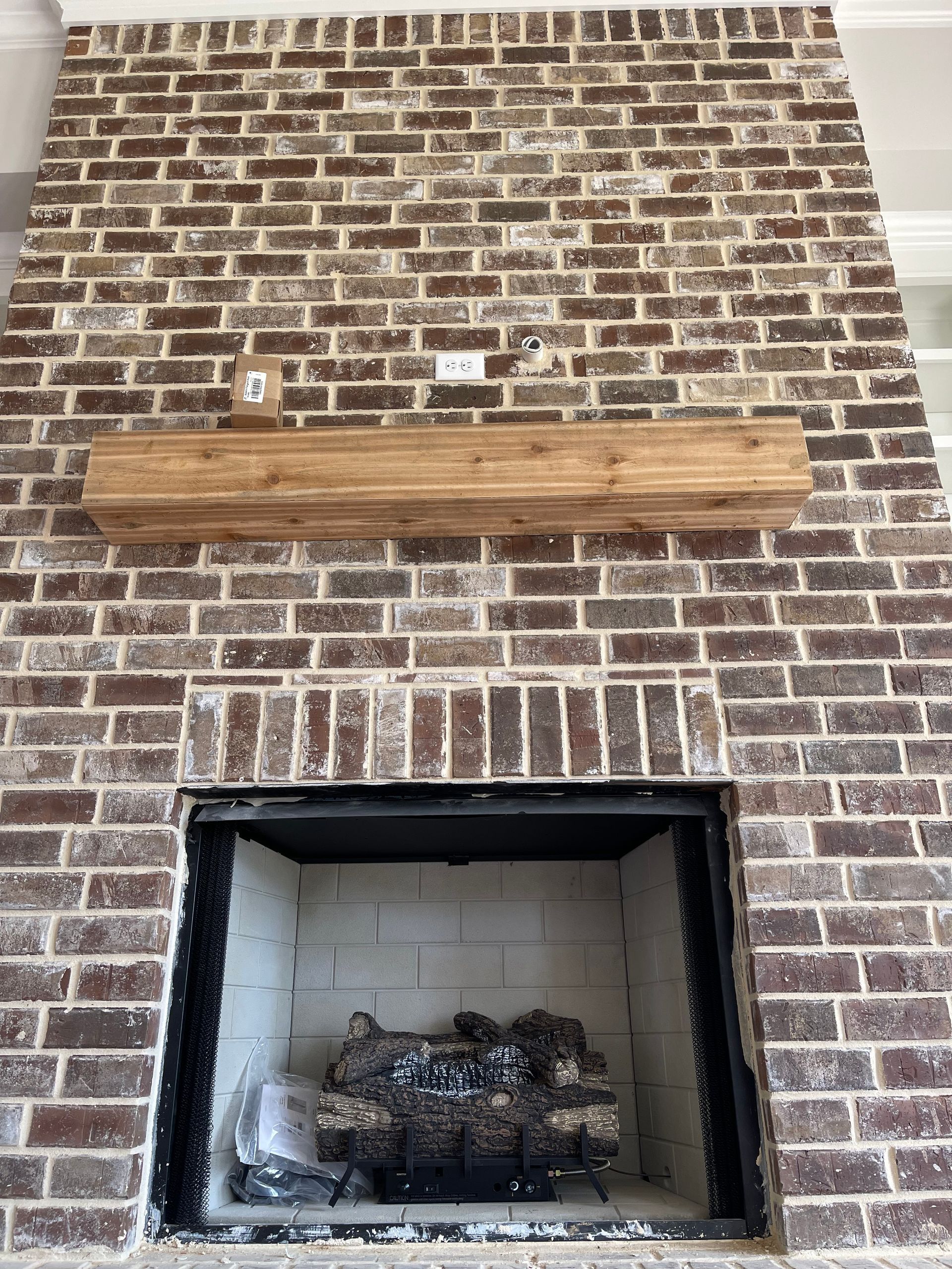 Brick fireplace with wooden mantel, featuring a dark interior and gas logs.