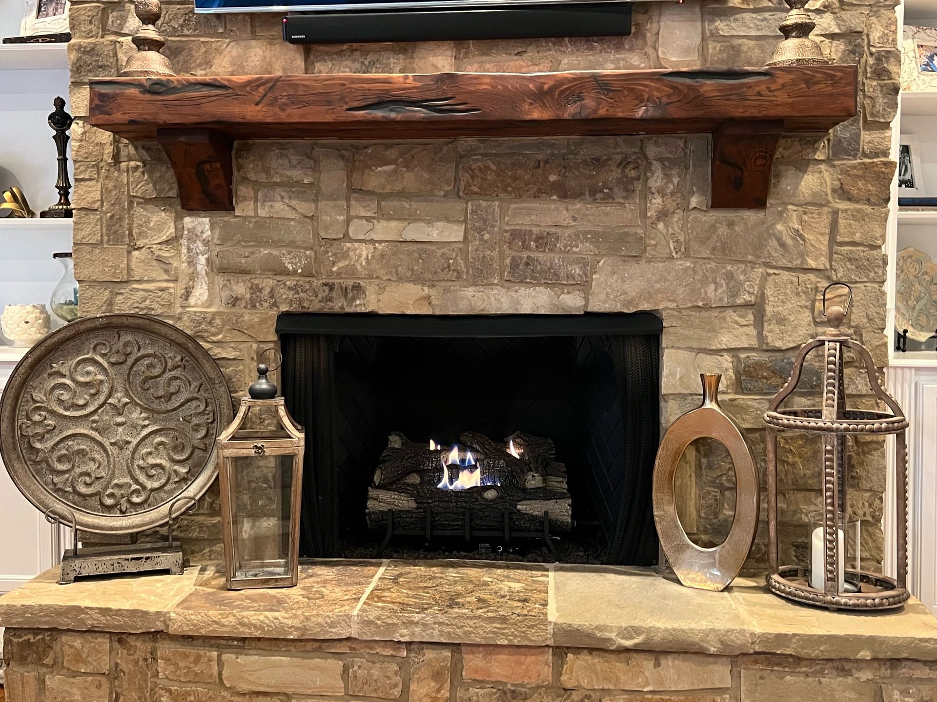 Fireplace with stone surround and wooden mantel, decorated with lanterns and a decorative tray.