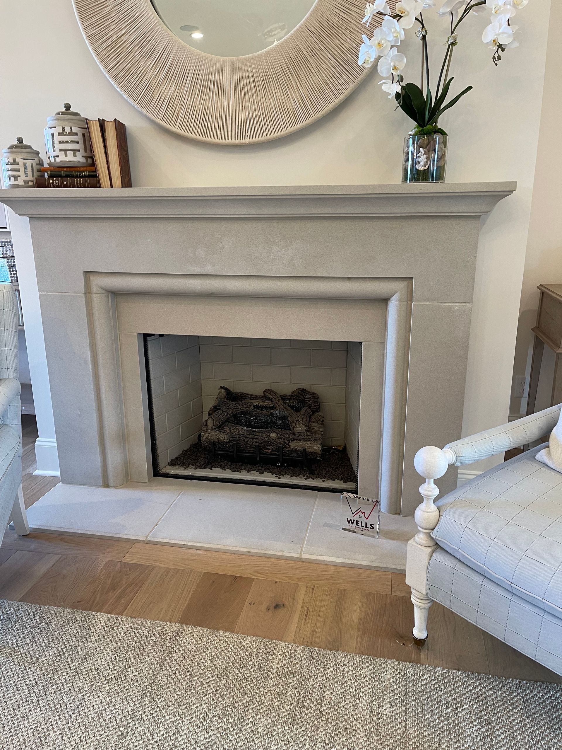 Fireplace with stone surround, artificial logs, and a decorative mirror and orchid.