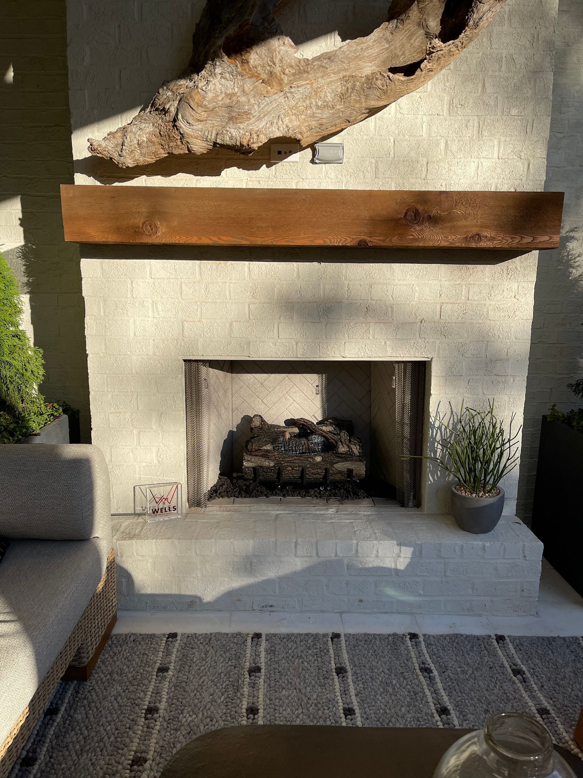 Outdoor fireplace with a wooden mantle and driftwood above.