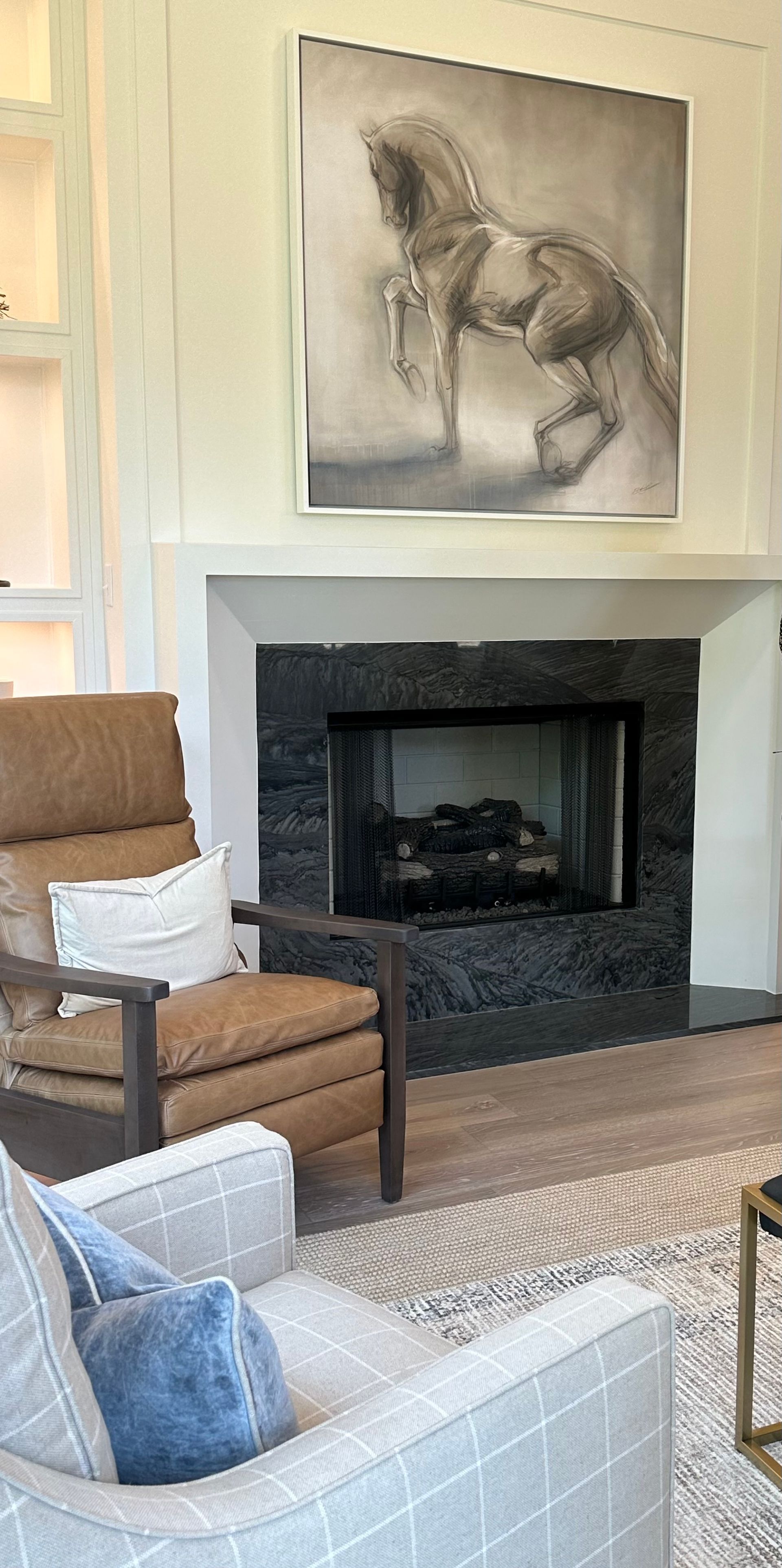 Living room with a fireplace, chairs, and a horse painting.