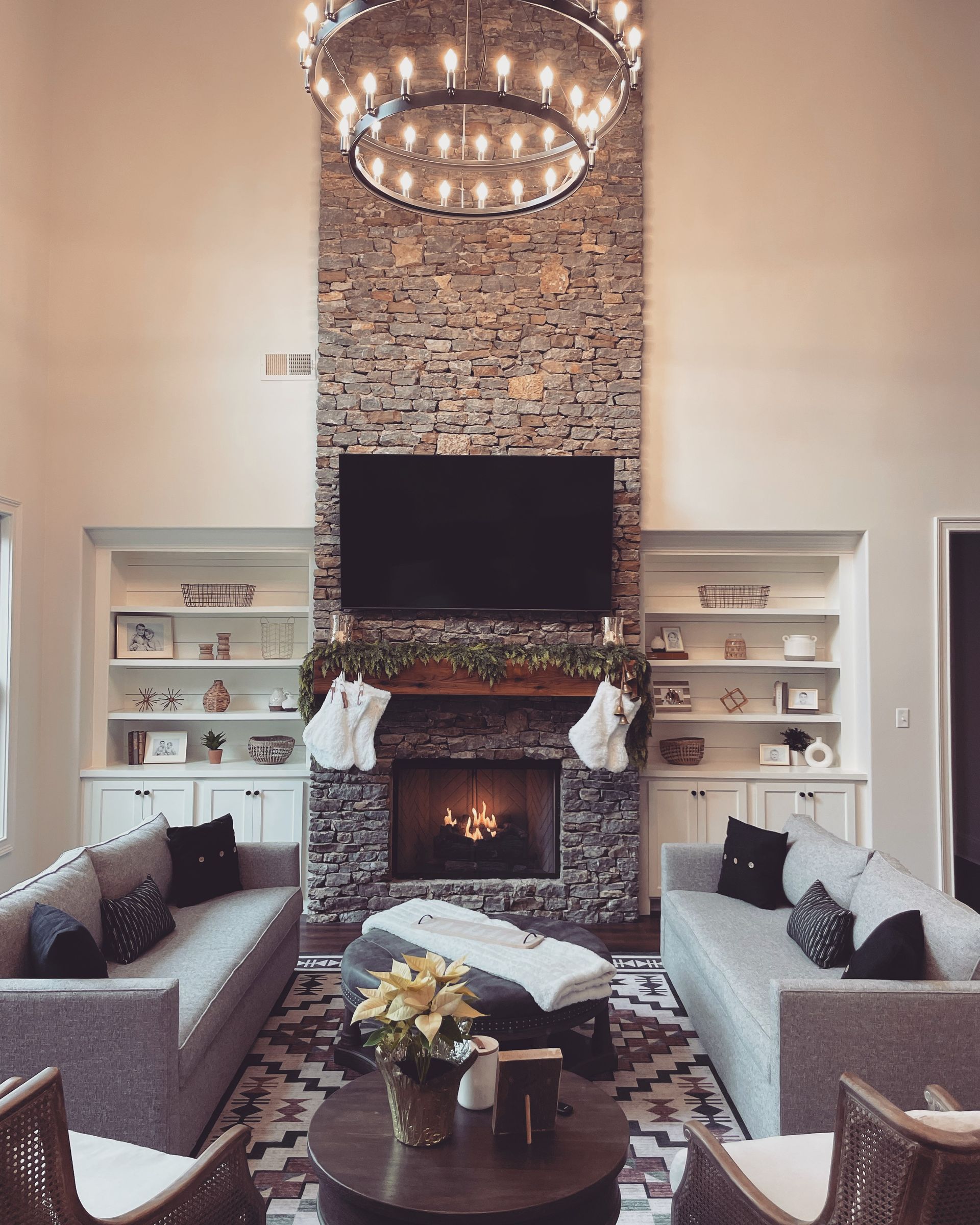 Living room with stone fireplace, TV, built-in shelves, couches, coffee table, and large chandelier.