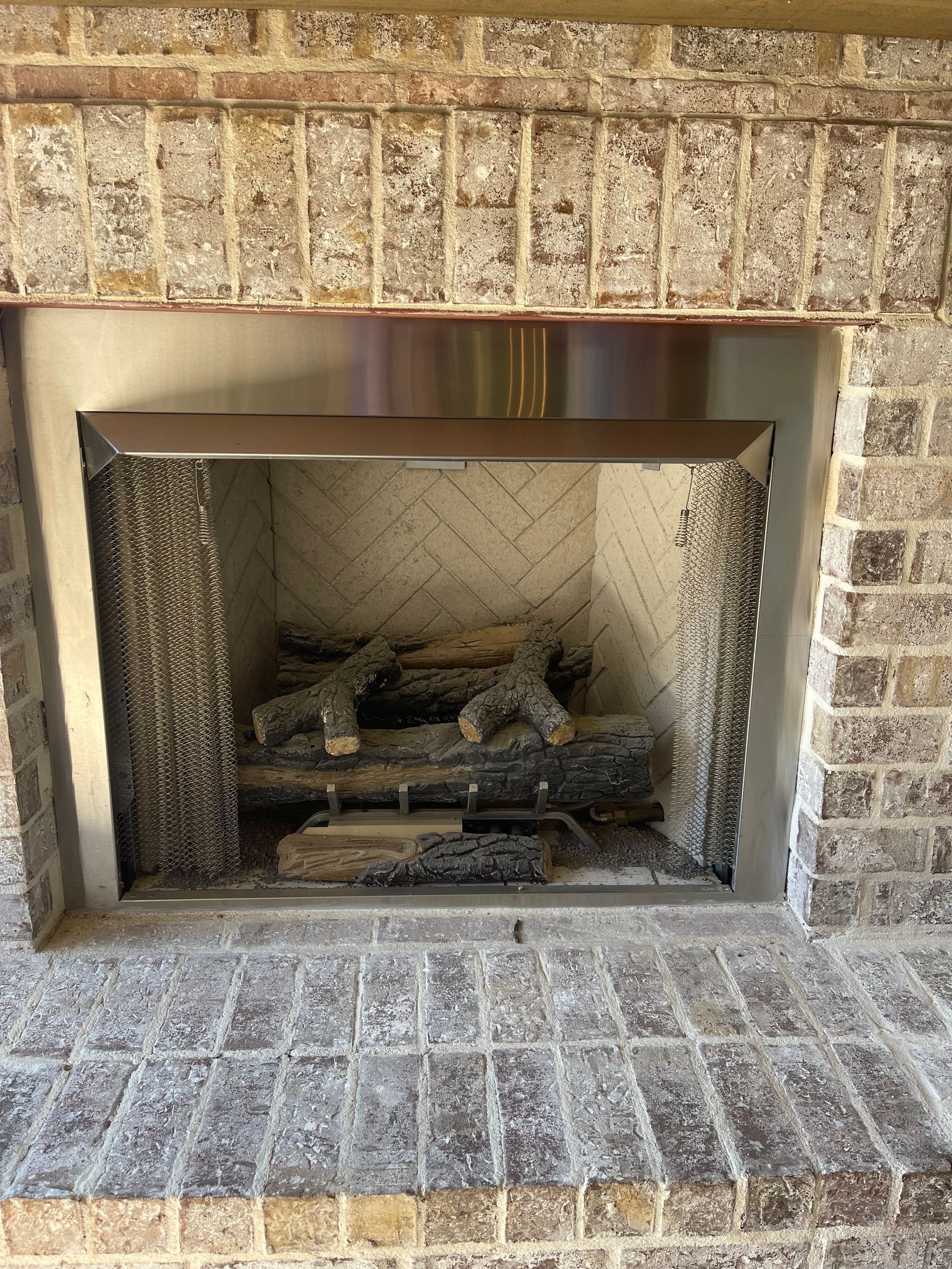 Brick fireplace with metal mesh screen and gas logs.