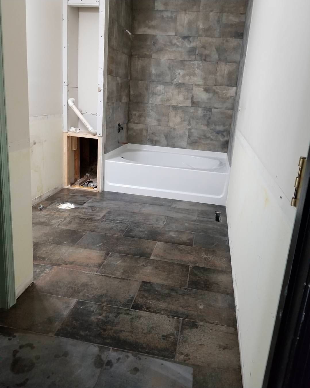 Bathroom under renovation: dark tile floor, gray stone-like shower tile, white tub, unfinished walls.
