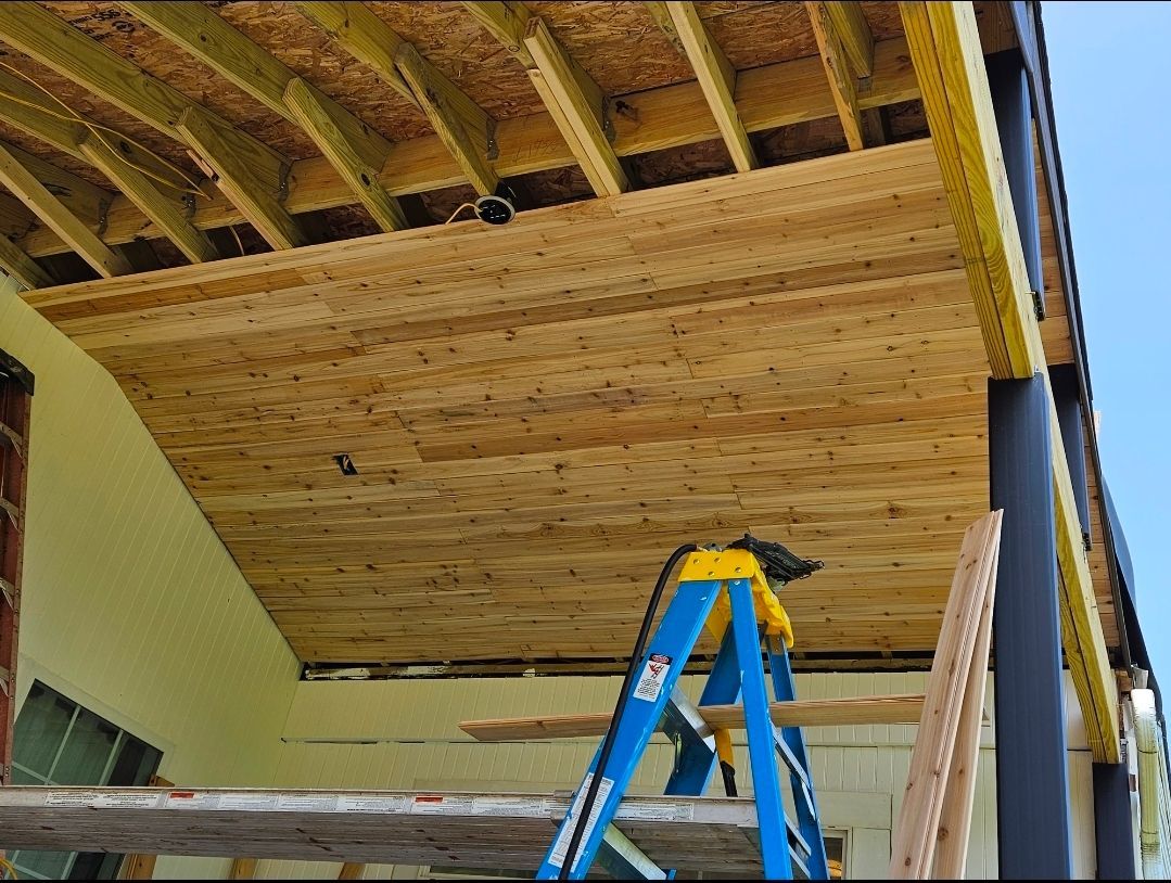 Construction of a porch roof, including wood framing and paneling, with a blue ladder visible.